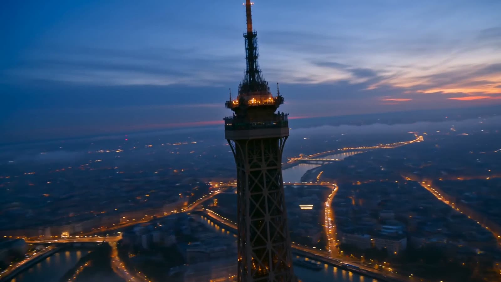 The illuminated tower at blue hour, aerial, Paris glowing below